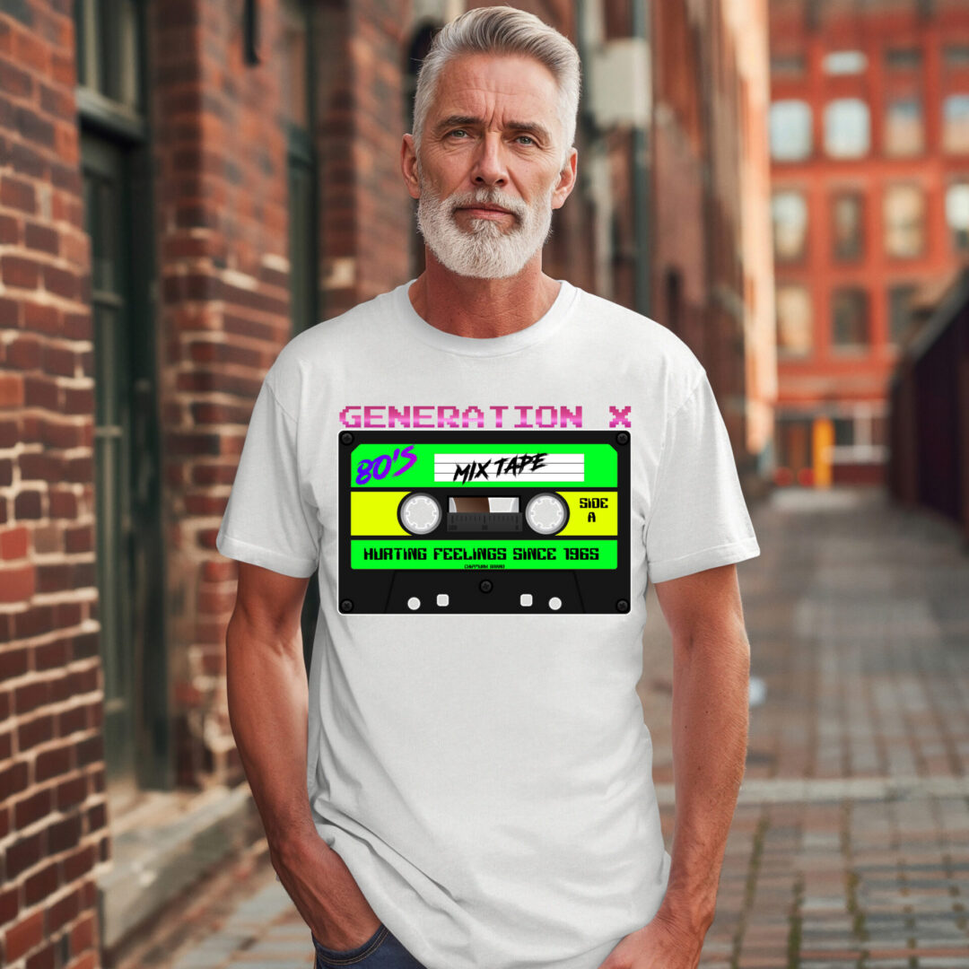 A man with gray hair and a beard stands outdoors wearing the Generation X Tape Tee, a white t-shirt with a colorful cassette tape graphic labeled "Generation X 80’s Mixtape" and "Hurting feelings since 1965.